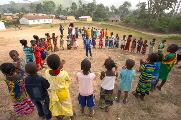 In Ebola-affected Guinea, children, supervised by an adult, play outdoors in a large circle in the village of Meliandou in Guéckédou Prefecture, Nzérékoré Region. Photo: UNICEF/Mark Naftalin
