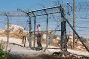 A settler security officer locking a gate in a fence separating Palestinians from their land | UN