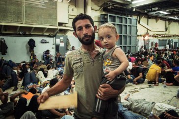 Onboard an Italian ship, a Syrian father holds his one-year-old son as they wait to be checked by doctors. They were rescued in the middle of the Mediterranean. Photo: UNHCR/A. D'Amato