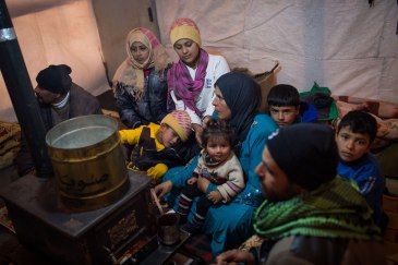 Members of a Syrian refugee family huddle around a stove inside their shelter in Lebanon’s Bekaa Valley. Photo: UNHCR/A. McConnell